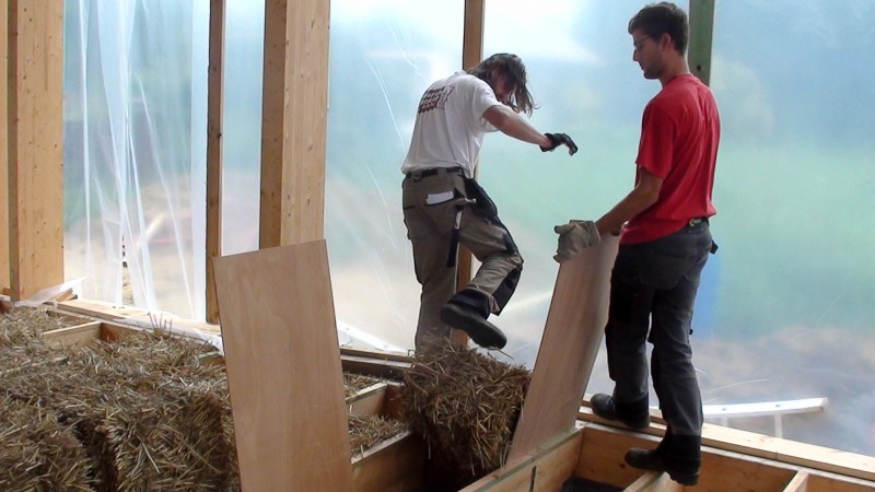 Terwijl Jens de triplex plank op haar plaats houdt, stampt Jean Marie de strobaal op zijn plaats.