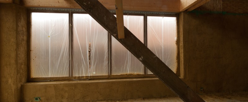 De muur van de eetkamer/living met afgeplakt raam en onze tijdelijke trap zoals hij er uitziet nadat de eerste leemlaag afgewerkt werd.