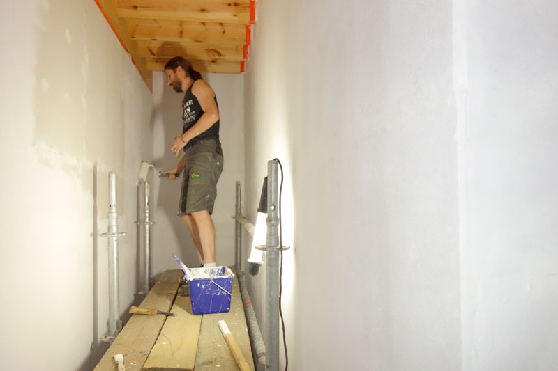 Op de stelling tussen de twee muren van de traphal is het een stuk makkelijker en veiliger werken dan op planken tussen twee ladders.