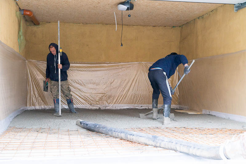 Terwijl met de neus van de betonpomp de beton op de juiste plaats gebracht wordt, strijkt één werkman de beton uit met een speciaal daarvoor gemaakte aftrekker.